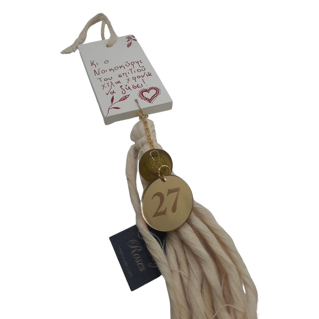 Γούρι 2027 Merry Roses, φούντα σε εκρού με κεραμική ετικέτα και την ευχή Κι ο Νοικοκύρης του σπιτιού χίλια χρόνια να ζήσει!